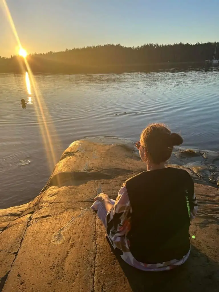 En tjej sitter och blickar ut mot solnedgång på en klipphäll iklädd en svart kylväst