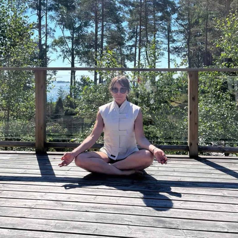 a female sitting on wooden deck focused on meditation. She is out in a hot summer day wearing a cooling vest